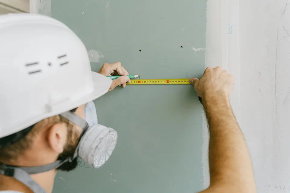 Profissional de capacete medindo uma parede de drywall com trena